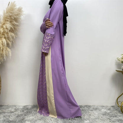 Frau in lila Abaya mit Spitzenärmeln, steht auf grauem Teppich. Dekorative Pflanzen im Hintergrund. Modest Fashion, islamische Kleidung.