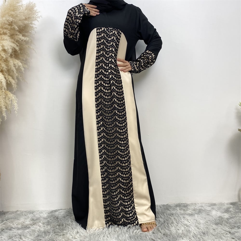 Schwarzes und cremefarbenes Maxikleid mit Spitzenmuster, langärmlig, auf grauem Teppich vor weißer Wand. Elegante Damenmode, islamische Kleidung.
