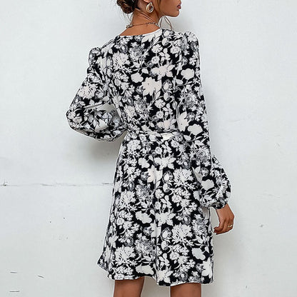 Frau in schwarz-weißem geblümtem Kleid mit langen Ärmeln, Rückansicht. Modetrend, elegantes Design, florales Muster, Damenbekleidung.