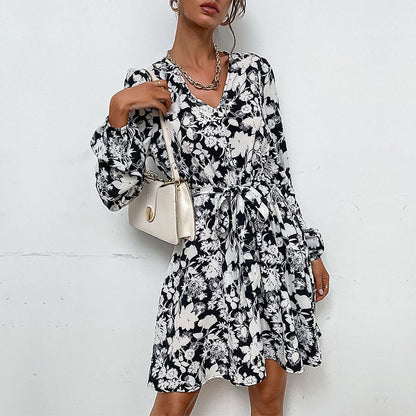 Frau in schwarz-weißem Blumenmuster-Kleid, trägt weiße Handtasche und silberne Halskette. Modetrend, elegantes Damenoutfit, stilvolle Kleidung.
