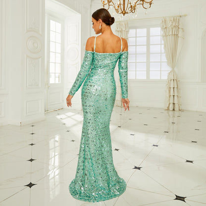 Frau in eleganter, schulterfreier, grüner Paillettenkleid, steht in luxuriösem, hellen Raum mit Kronleuchter und Marmorboden, Rückansicht.