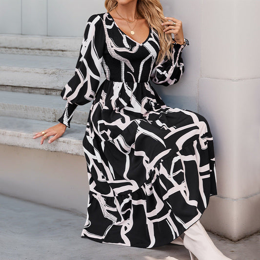 Frau in schwarz-weiß gemustertem Maxikleid mit langen Ärmeln sitzt auf Treppe. Modetrend, elegantes Design, stilvolle Damenbekleidung.