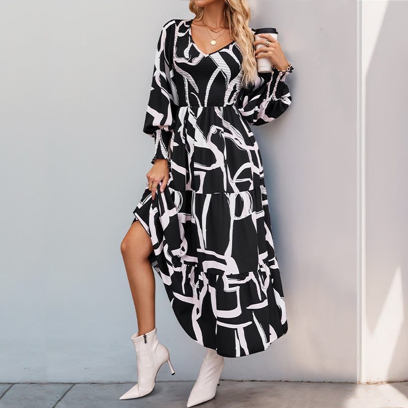 Frau in schwarz-weißem Maxikleid mit abstraktem Muster, trägt weiße Stiefeletten, steht an einer Wand. Modetrend, elegantes Damenoutfit, Herbstmode.
