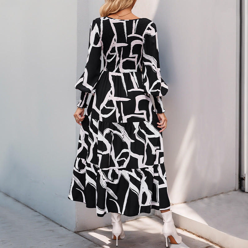 Frau in langem, schwarz-weiß gemustertem Kleid mit langen Ärmeln und weißen Stiefeletten, steht vor einer grauen Wand. Modetrend, Damenmode, Herbstkleid.