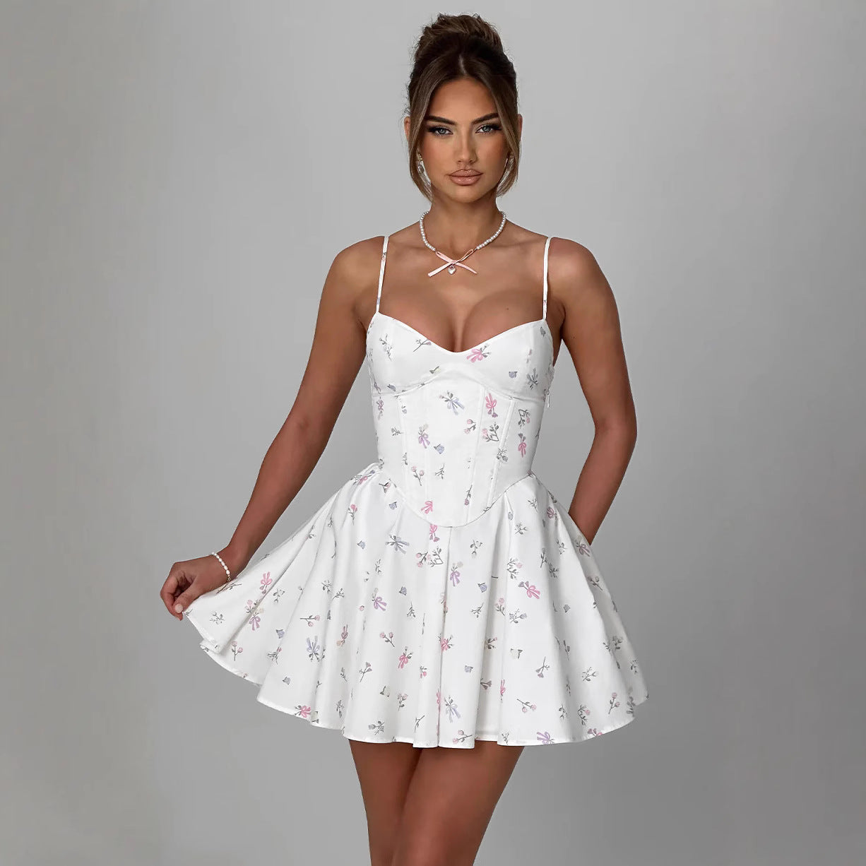 Frau in weißem, geblümtem Sommerkleid mit Spaghettiträgern vor grauem Hintergrund. Modetrend, elegantes Damenoutfit, stilvolle Sommermode.