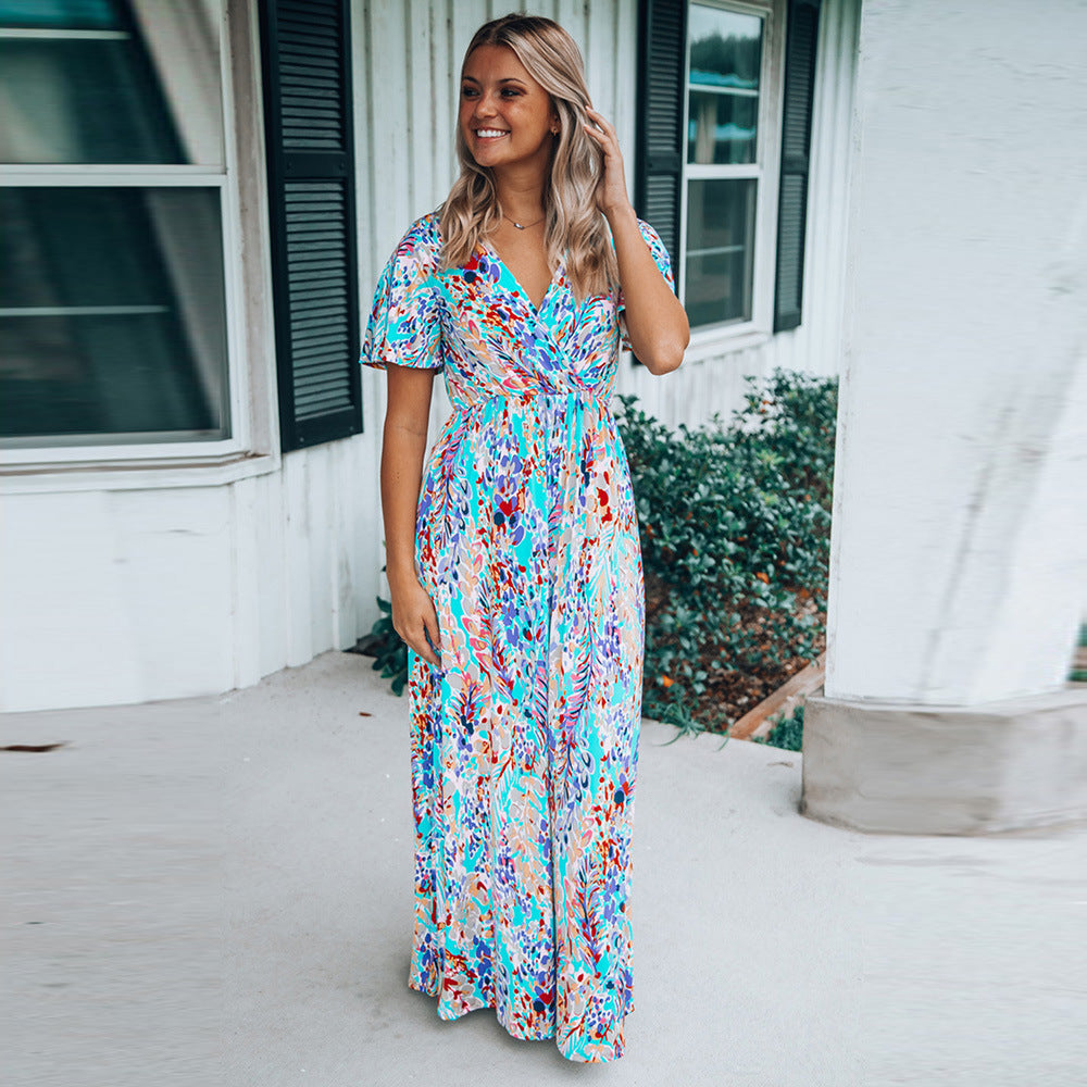 Frau in langem, buntem Sommerkleid steht auf Veranda vor weißem Haus mit grünen Fensterläden. Mode, Sommerkleid, Damenmode, Veranda.