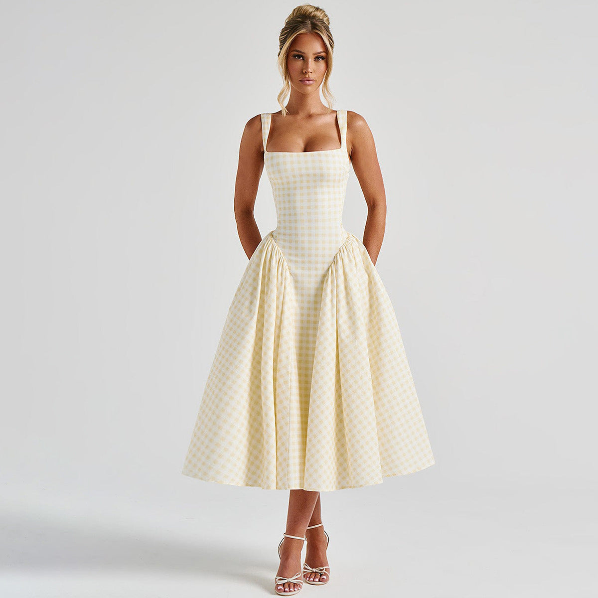 Frau in kariertem Sommerkleid, knielang, mit Spaghettiträgern, posiert vor neutralem Hintergrund. Elegante Mode, zeitloser Stil, Damenbekleidung.