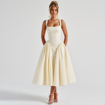 Frau in kariertem Sommerkleid, knielang, mit Spaghettiträgern, posiert vor neutralem Hintergrund. Elegante Mode, zeitloser Stil, Damenbekleidung.