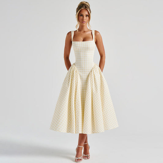 Frau in kariertem Sommerkleid, knielang, mit Spaghettiträgern, posiert vor neutralem Hintergrund. Elegante Mode, zeitloser Stil, Damenbekleidung.
