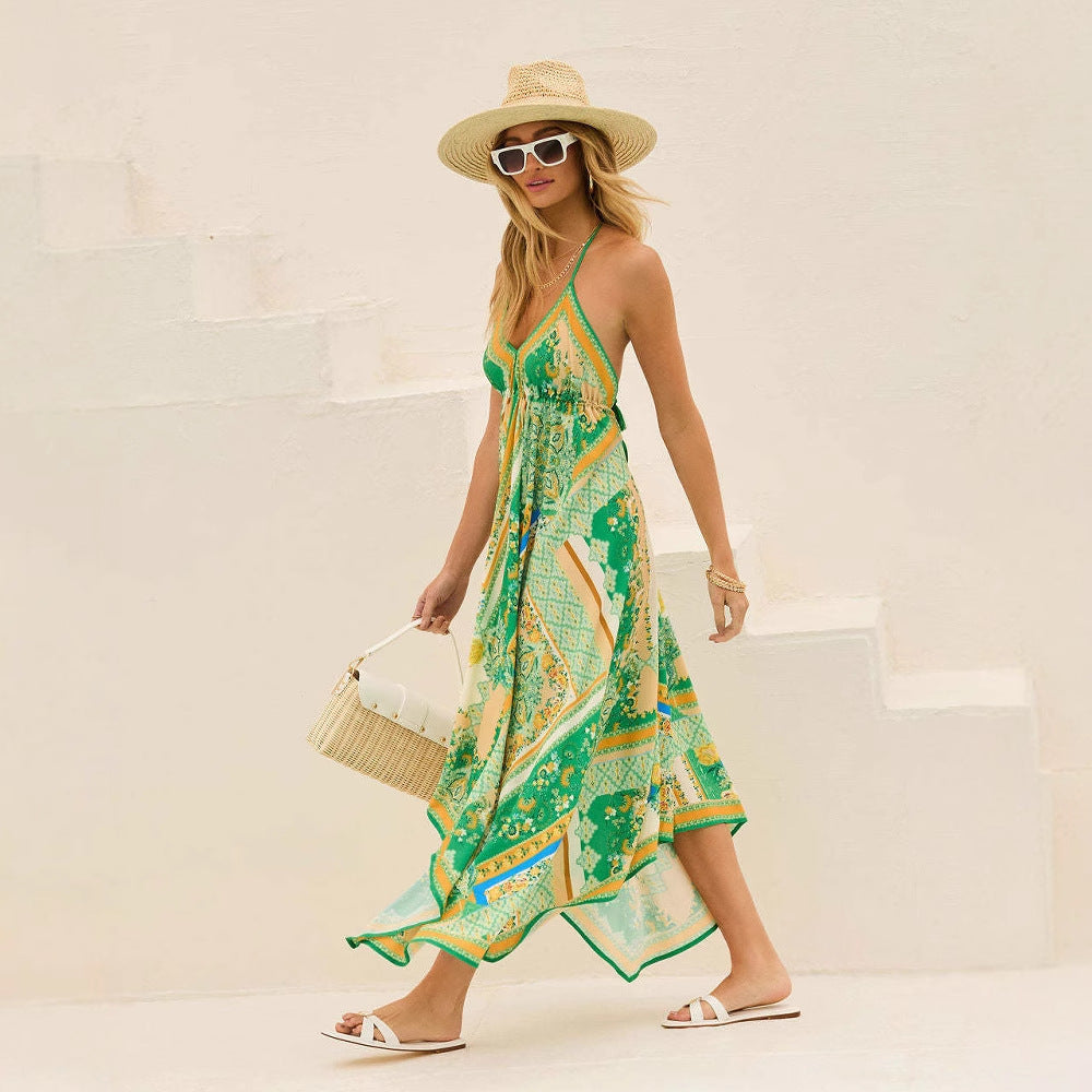 Frau in grünem Sommerkleid mit Muster, Strohhut und Sonnenbrille, geht eine weiße Treppe hinunter, trägt eine beige Handtasche und weiße Sandalen.