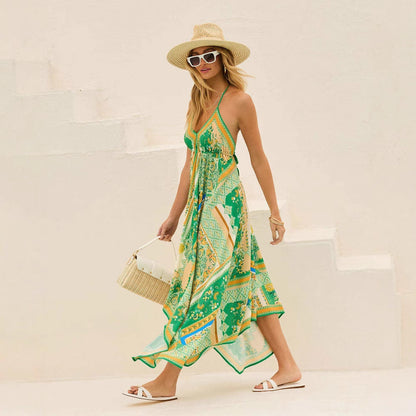 Frau in grünem Sommerkleid mit Muster, Strohhut und Sonnenbrille, geht eine weiße Treppe hinunter, trägt eine beige Handtasche und weiße Sandalen.