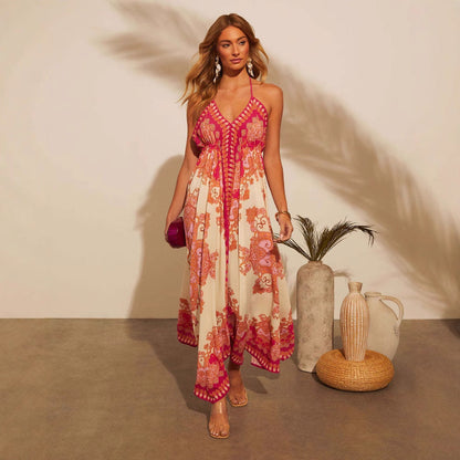 Frau in einem eleganten, geblümten Sommerkleid mit rosa und orangefarbenen Mustern, steht neben dekorativen Vasen auf grauem Boden.