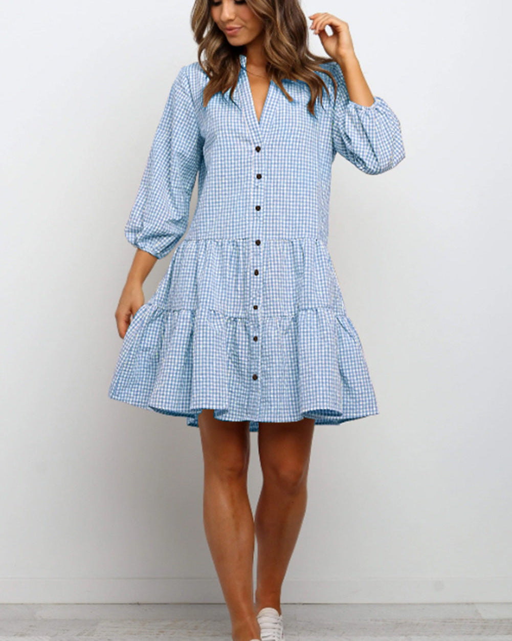 Frau in blau-weiß kariertem Hemdblusenkleid mit Knopfleiste und Puffärmeln, modisches Sommeroutfit, Freizeitkleidung, stehend vor weißem Hintergrund.