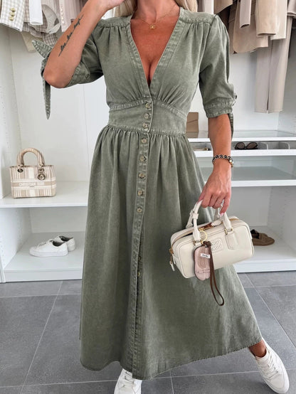 Frau in olivgrünem Kleid mit Knopfleiste, hält cremefarbene Handtasche, trägt weiße Sneaker. Mode, Damenbekleidung, eleganter Look.
