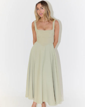 Frau in elegantem, ärmellosem, hellgrünem Midikleid mit quadratischem Ausschnitt, stehend vor weißem Hintergrund. Mode, Damenkleidung, Sommerkleid.