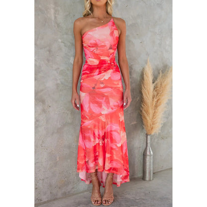 Frau in einem schulterfreien, roten Blumenkleid vor grauer Wand, neben Pampasgras in Vase. Elegantes Sommeroutfit, modisches Abendkleid.