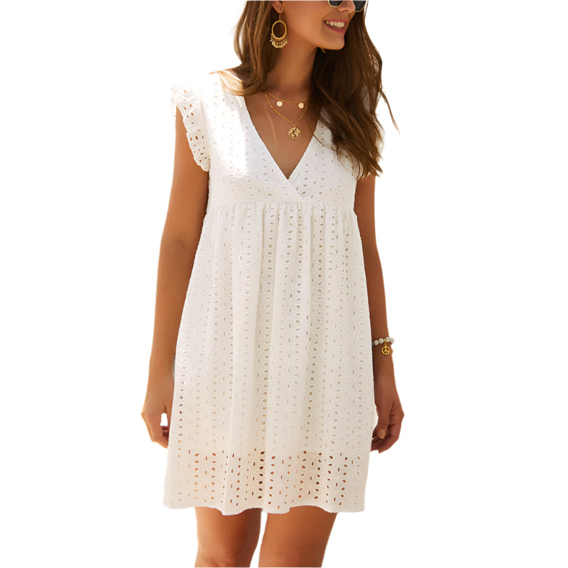Frau in weißem Sommerkleid mit Lochstickerei, V-Ausschnitt und Rüschenärmeln, trägt goldene Ohrringe und Armbänder. Ideal für Sommermode.