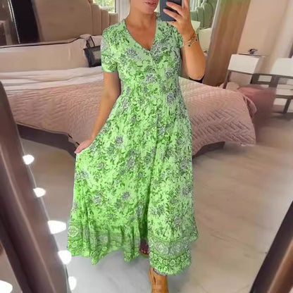 Frau in grünem, geblümtem Maxikleid posiert vor Spiegel im Schlafzimmer. Sommermode, elegantes Design, florales Muster, trendiges Outfit.