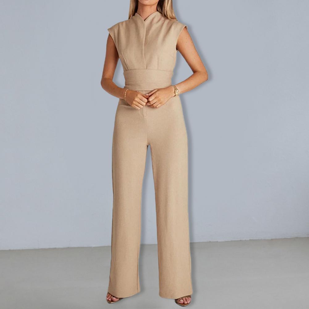 Frau in eleganter, ärmelloser, beigefarbener Jumpsuit vor grauem Hintergrund. Modetrend, Damenbekleidung, stilvolles Outfit.