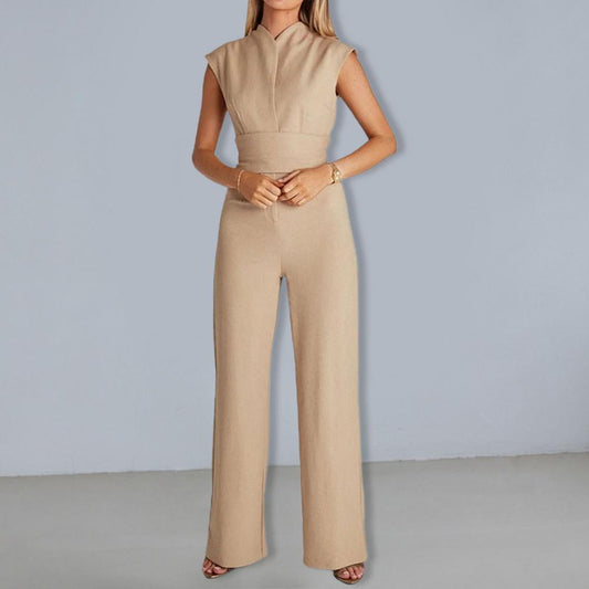 Frau in eleganter, ärmelloser, beigefarbener Jumpsuit vor grauem Hintergrund. Modetrend, Damenbekleidung, stilvolles Outfit.