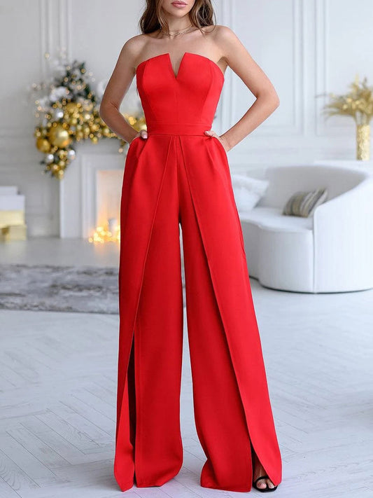Frau in elegantem roten Jumpsuit in modernem Wohnzimmer mit Weihnachtsdekoration, goldenen Akzenten und weißem Sofa im Hintergrund.