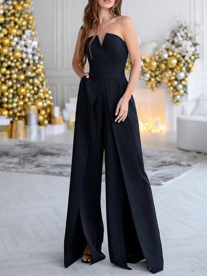 Elegantes schwarzes Abendkleid, trägerlos, mit weitem Bein, vor festlich geschmücktem Weihnachtsbaum. Perfekt für festliche Anlässe und Partys.