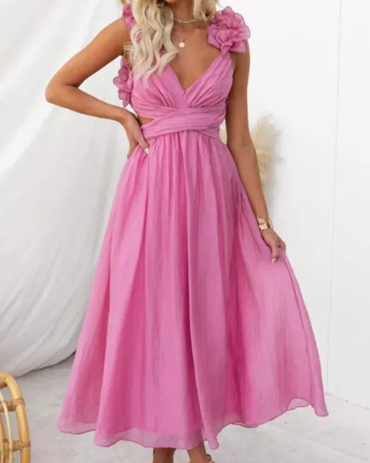 Frau in rosa Sommerkleid mit V-Ausschnitt und Blumenapplikationen, posiert vor weißem Hintergrund. Elegantes, luftiges Design für warme Tage.