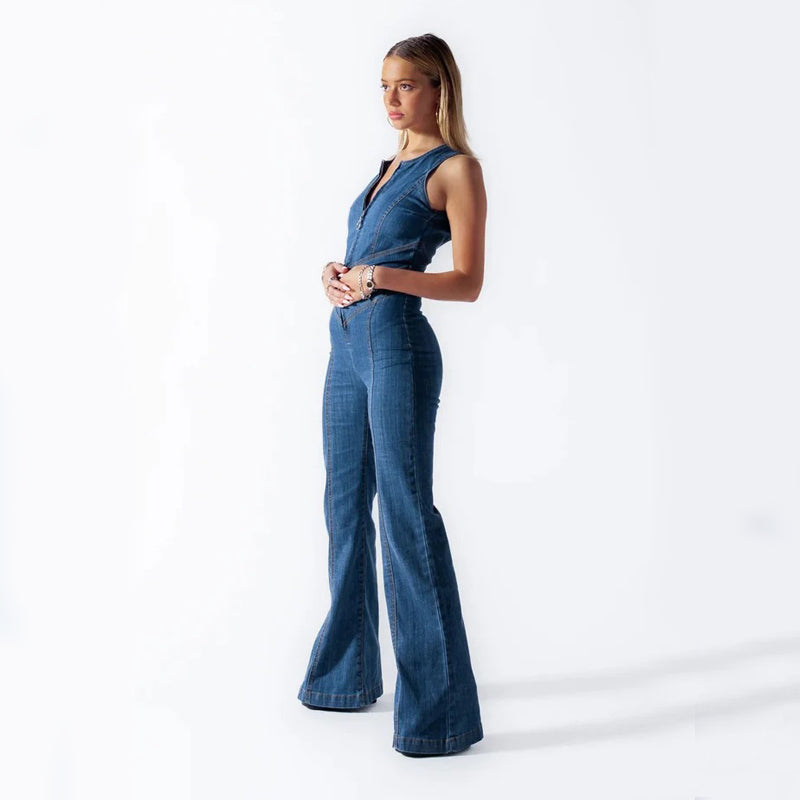Frau in blauem Jeans-Jumpsuit, stehend vor weißem Hintergrund. Modetrend, Damenbekleidung, eleganter Look, Denim-Mode, Ganzkörperaufnahme.