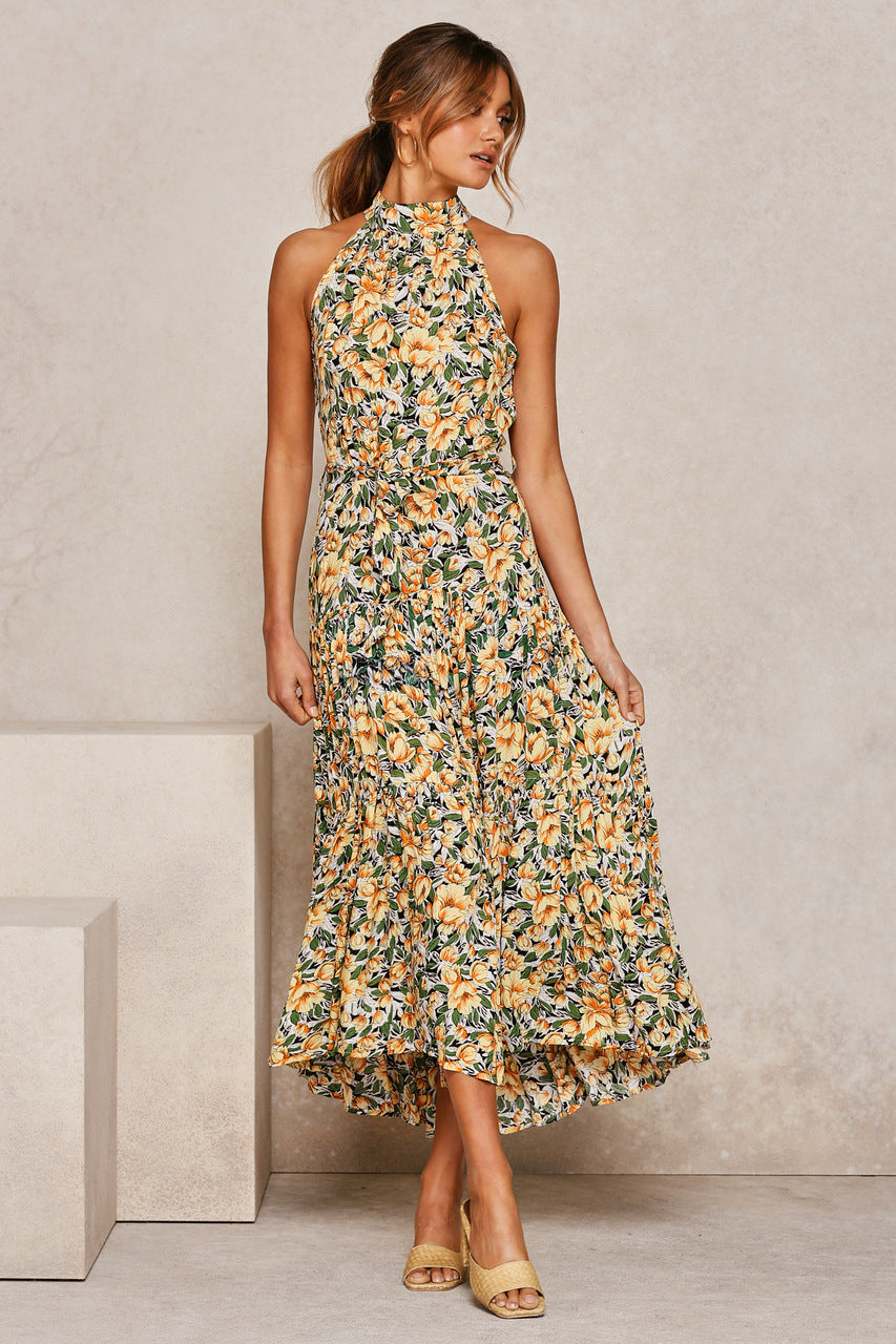 Frau in geblümtem Maxikleid mit gelben und grünen Mustern, ärmellos, mit Stehkragen, posiert vor neutralem Hintergrund. Elegante Sommermode.