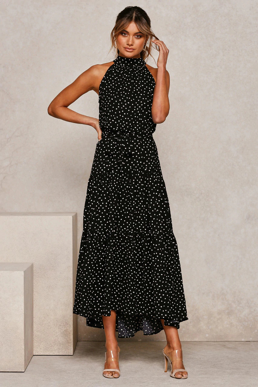 Frau in schwarzem, ärmellosem Maxikleid mit weißen Punkten, posiert vor neutralem Hintergrund. Elegante Mode, Sommerkleid, Damenbekleidung.