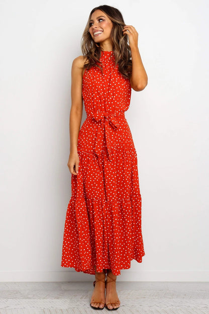 Frau in rotem, ärmellosem Maxikleid mit weißen Punkten, lächelt und steht vor weißem Hintergrund. Sommermode, elegantes Design, Freizeitkleidung.