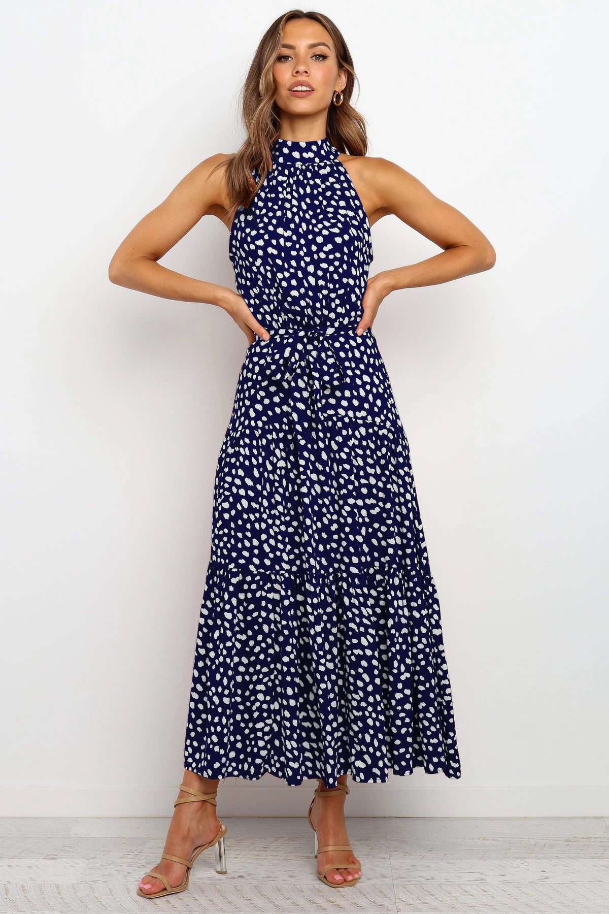 Frau in blau-weiß gepunktetem Maxikleid, ärmellos, mit Stehkragen, posiert vor weißem Hintergrund. Elegantes Sommeroutfit, Mode, Damenkleidung.