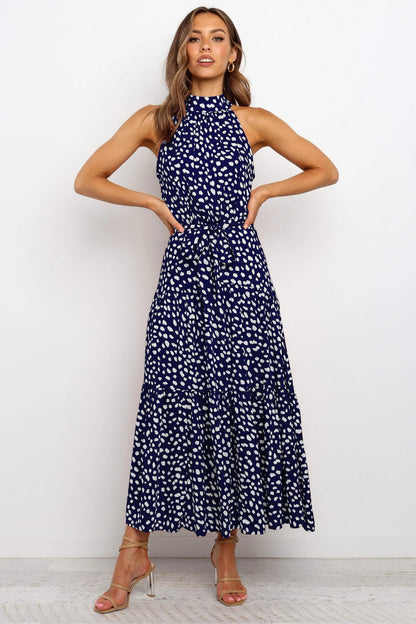 Frau in blau-weiß gepunktetem Maxikleid, ärmellos, mit Stehkragen, posiert vor weißem Hintergrund. Elegantes Sommeroutfit, Mode, Damenkleidung.
