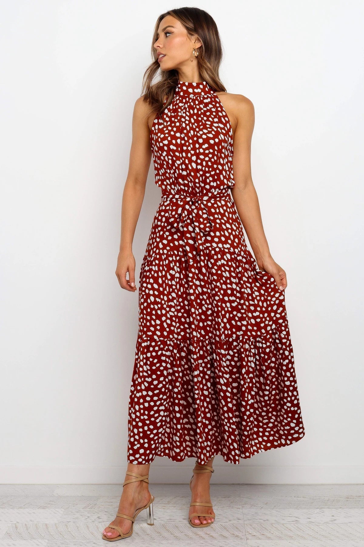 Frau in rotem, gepunktetem Maxikleid, ärmellos, mit Halterneck, posiert vor weißem Hintergrund. Elegantes Sommeroutfit, Mode, Damenbekleidung.