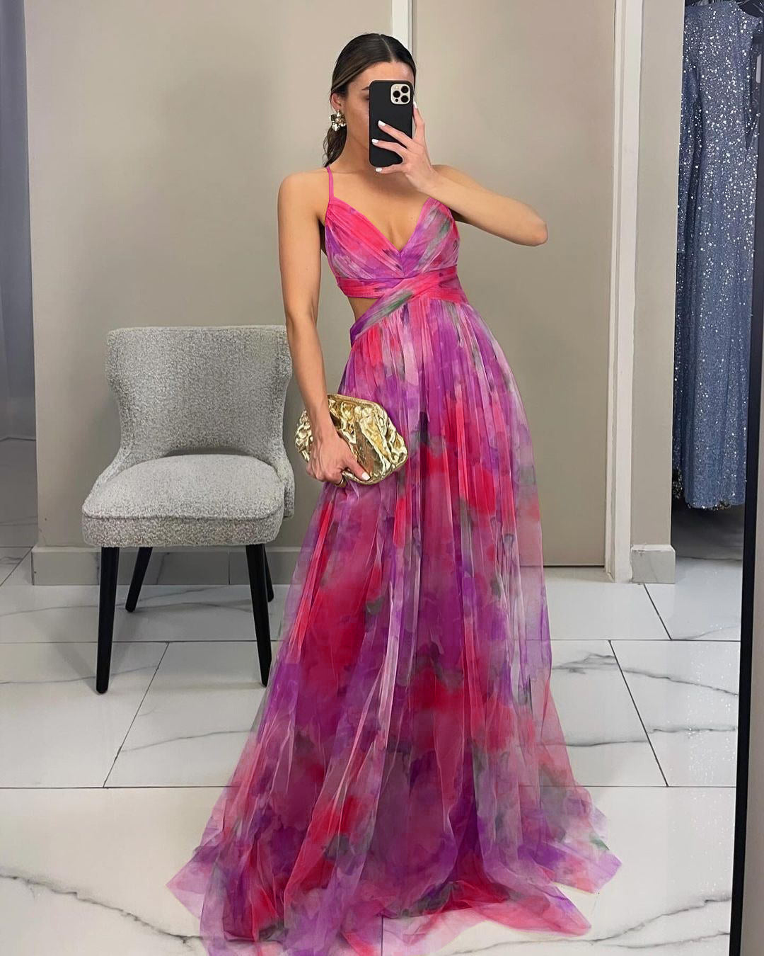 Frau in elegantem, langem, pink-lila Abendkleid mit Blumenmuster, hält goldene Clutch, macht Selfie im Spiegel. Perfekt für Gala oder Ball.