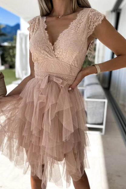 Frau in elegantem, rosa Spitzenkleid mit Tüllrock, V-Ausschnitt und Schleife, steht auf Terrasse. Perfekt für Sommermode und Abendveranstaltungen.