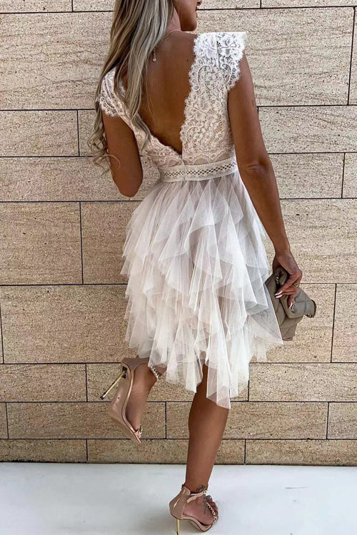 Frau in weißem Spitzenkleid mit Tüllrock, Rückansicht, vor beiger Steinwand, hält eine kleine Tasche, elegante Abendmode, Sommerkleid.