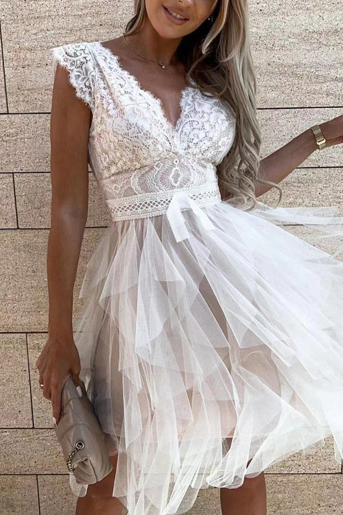 Frau in elegantem weißen Spitzenkleid mit Tüllrock, hält eine beige Handtasche. Perfekt für Hochzeiten oder festliche Anlässe.