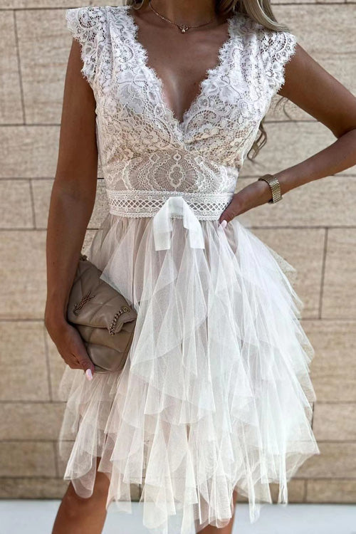 Frau in elegantem, weißem Spitzenkleid mit V-Ausschnitt und Tüllrock, hält eine beige Clutch. Perfekt für Hochzeiten oder festliche Anlässe.