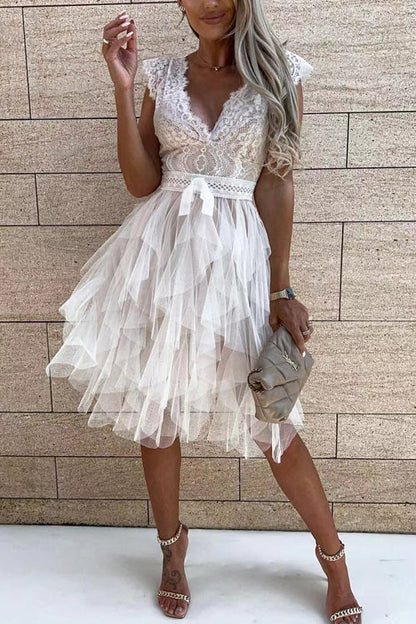 Frau in elegantem, weißem Spitzenkleid mit Rüschen, steht vor einer Steinwand. Perfekt für Sommermode, Abendveranstaltungen, stilvolle Outfits.