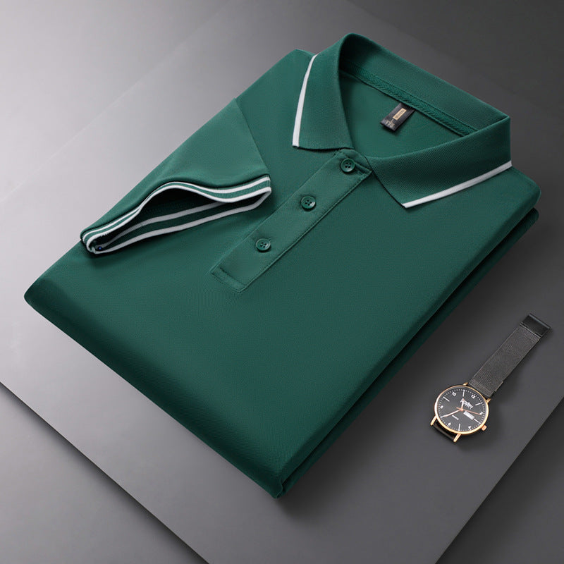 Gefaltetes grünes Polohemd mit weißem Kragen auf grauem Hintergrund, daneben eine elegante Armbanduhr. Mode, Herrenbekleidung, Accessoires.