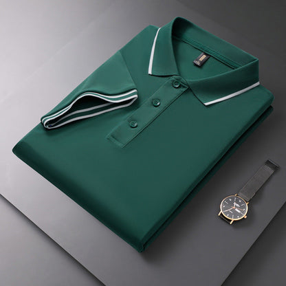 Gefaltetes grünes Polohemd mit weißem Kragen auf grauem Hintergrund, daneben eine elegante Armbanduhr. Mode, Herrenbekleidung, Accessoires.