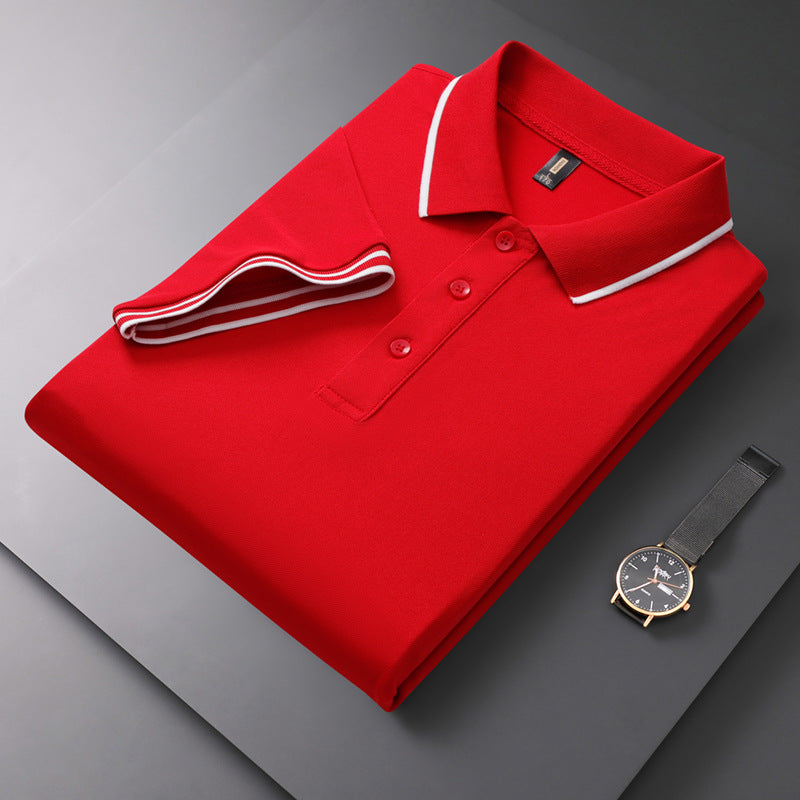 Gefaltetes rotes Polohemd mit weißem Kragen auf grauem Hintergrund, daneben eine elegante Armbanduhr. Mode, Herrenbekleidung, Accessoires.