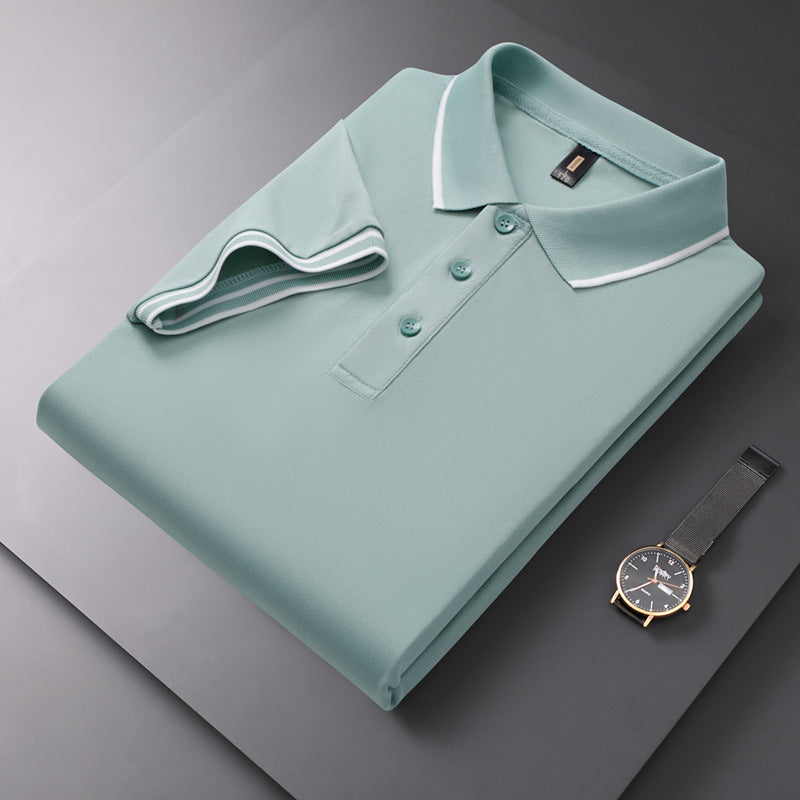 Gefaltetes grünes Polohemd mit Knopfleiste und weißem Kragen auf grauem Hintergrund, neben einer eleganten Armbanduhr. Mode, Herrenbekleidung, Accessoires.