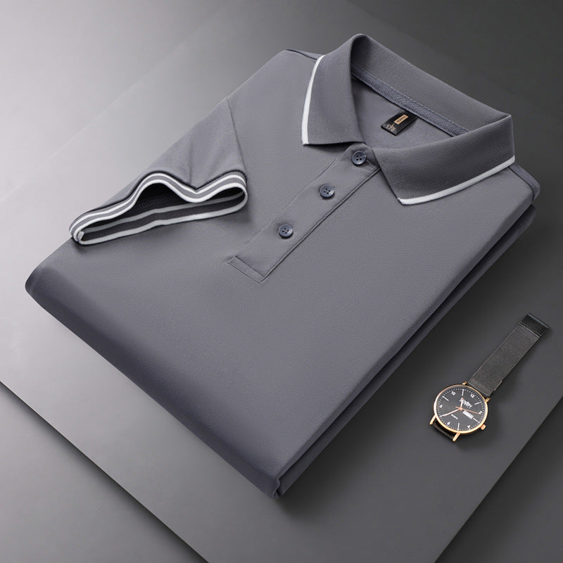 Graues Polohemd mit Knopfleiste und weißem Kragen, elegant gefaltet auf grauem Hintergrund. Daneben liegt eine stilvolle Armbanduhr.