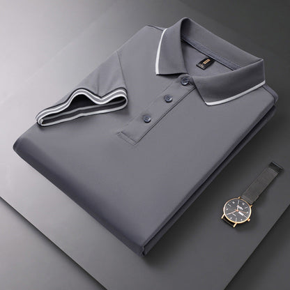 Graues Polohemd mit Knopfleiste und weißem Kragen, elegant gefaltet auf grauem Hintergrund. Daneben liegt eine stilvolle Armbanduhr.