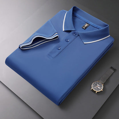 Gefaltetes blaues Polohemd mit weißen Akzenten auf grauem Hintergrund, daneben eine elegante Armbanduhr. Mode, Herrenbekleidung, Accessoires.