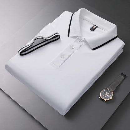 Gefaltetes weißes Polohemd mit schwarzem Kragen und Knopfleiste, daneben eine elegante Armbanduhr auf grauem Hintergrund.