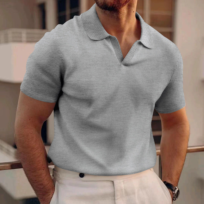 Mann in grauem Polohemd und weißer Hose auf Balkon. Sommermode, Herrenbekleidung, stilvoll, modern, Freizeitlook, urbane Kulisse.