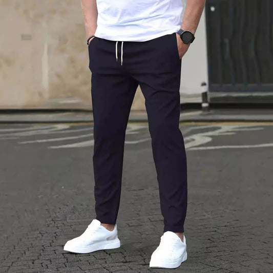 Mann in dunkelblauer Jogginghose und weißen Sneakers auf Asphalt. Lässige Herrenmode, Streetwear, bequeme Freizeitkleidung.
